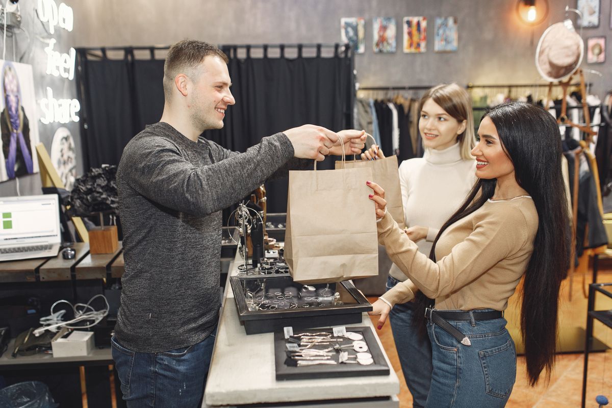 Small Business Customer Service Tips: A Simple Guide That Keeps Customers Coming Back 42 Friendly shop assistant handing shopping bags to happy customers at a small shop counter